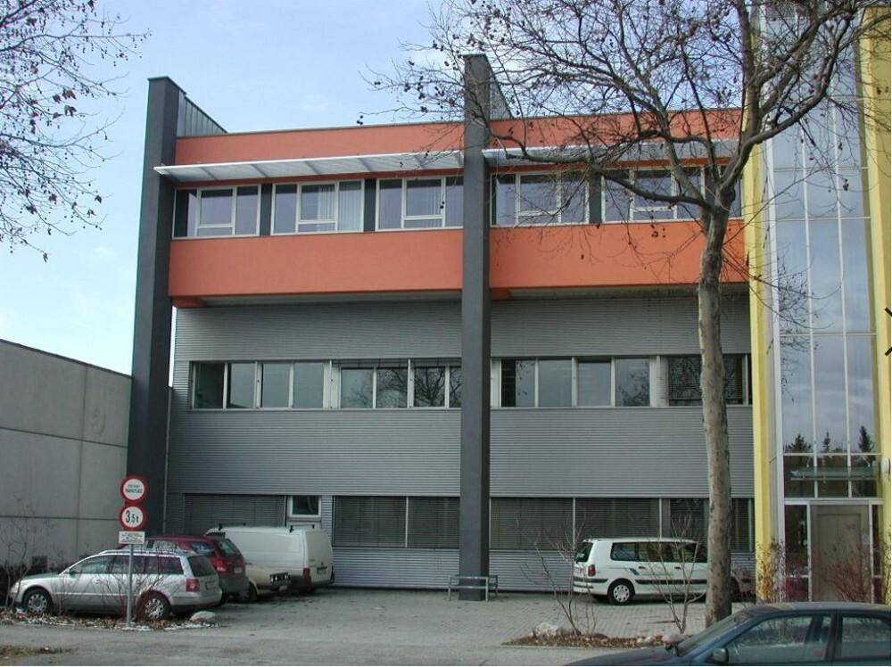 Ansicht eines modernen Geschäftsgebäudes mit farbiger Fassade und Parkplätzen davor.
