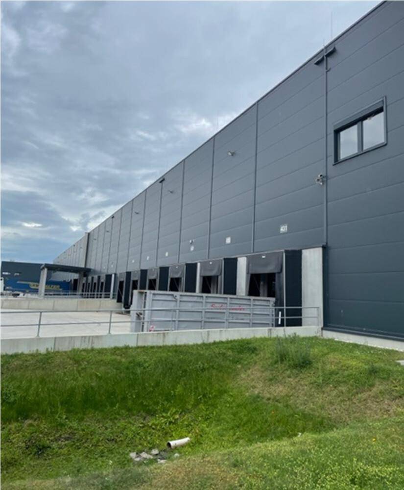 Moderne Lagerhalle mit mehreren Laderampen und grauer Fassadenverkleidung unter bewölktem Himmel.