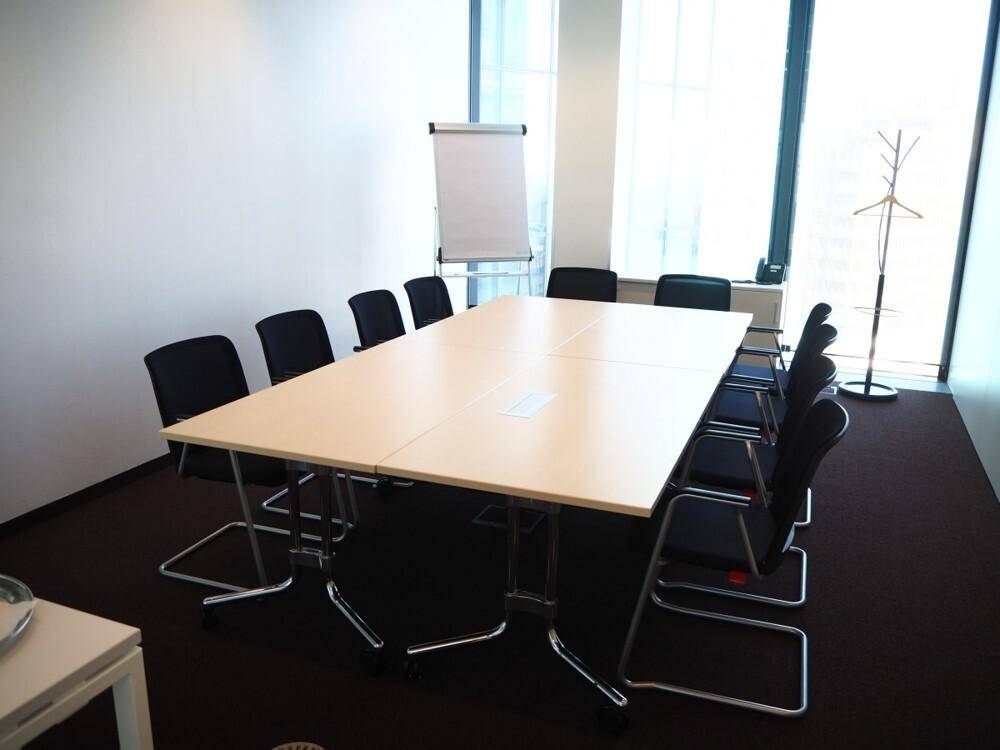 Geräumiger Konferenzraum mit langem Tisch, vielen Stühlen und einem Whiteboard.