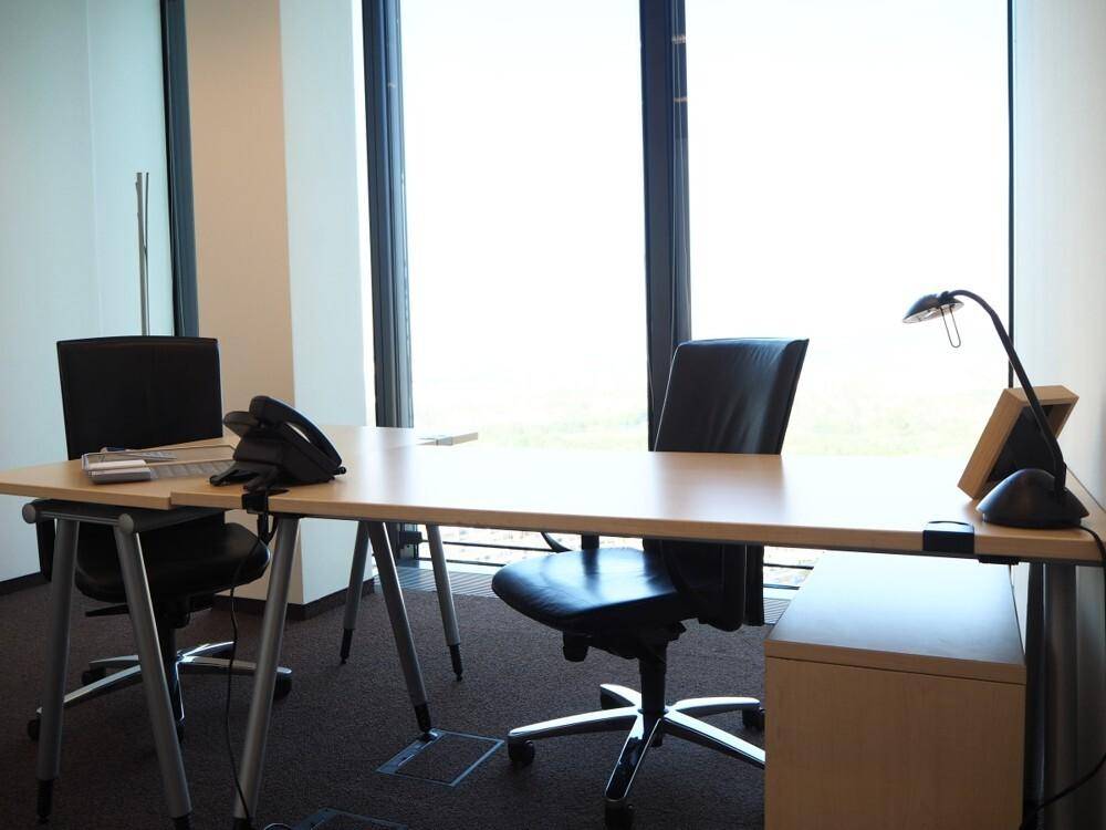 Heller Büroraum mit modernem Schreibtisch, Bürostühlen und großen Fenstern.