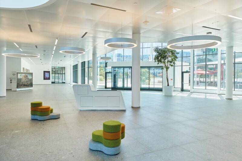 Geräumige, moderne Lobby mit hohen Decken, runden Leuchten und farbenfrohen Sitzgelegenheiten.