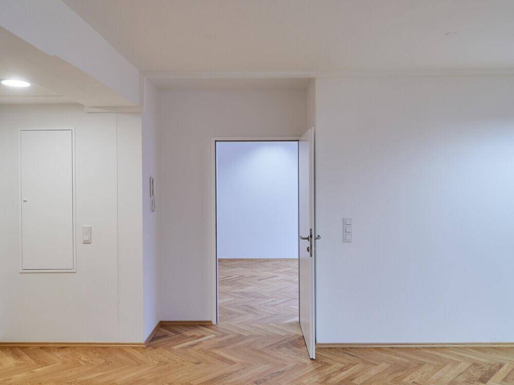 Heller Flur mit Fischgrätparkett und weiß gestrichenen Wänden, der zu weiteren Räumen führt.