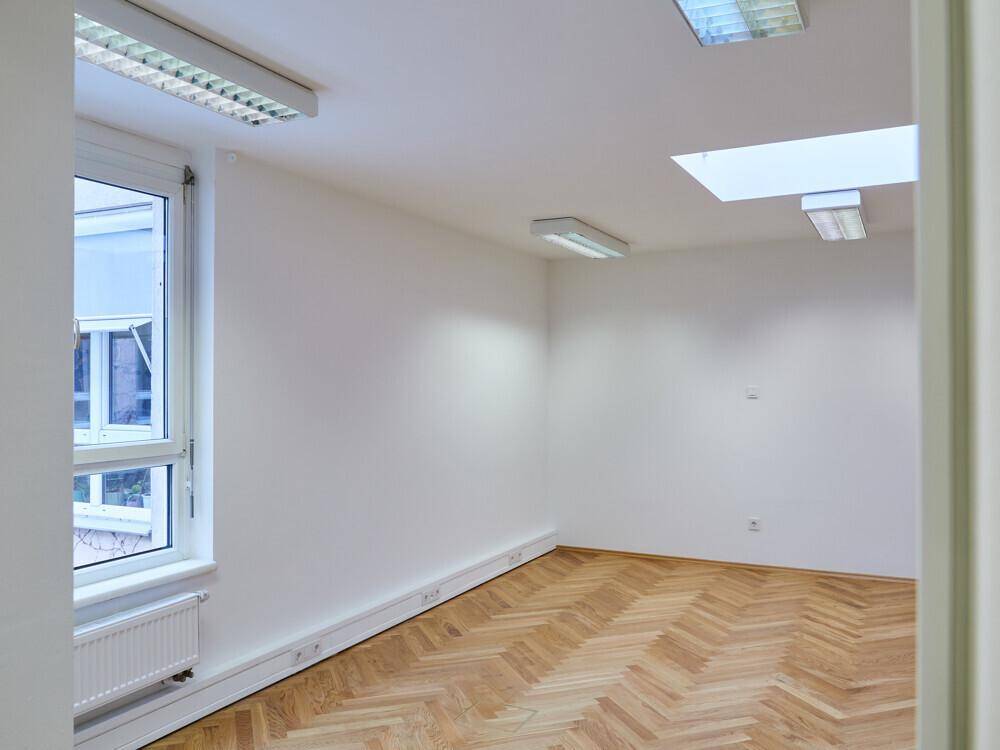 Kleiner, heller Büroraum mit Fischgrätparkett, einem Fenster und einem rechteckigen Dachfenster.