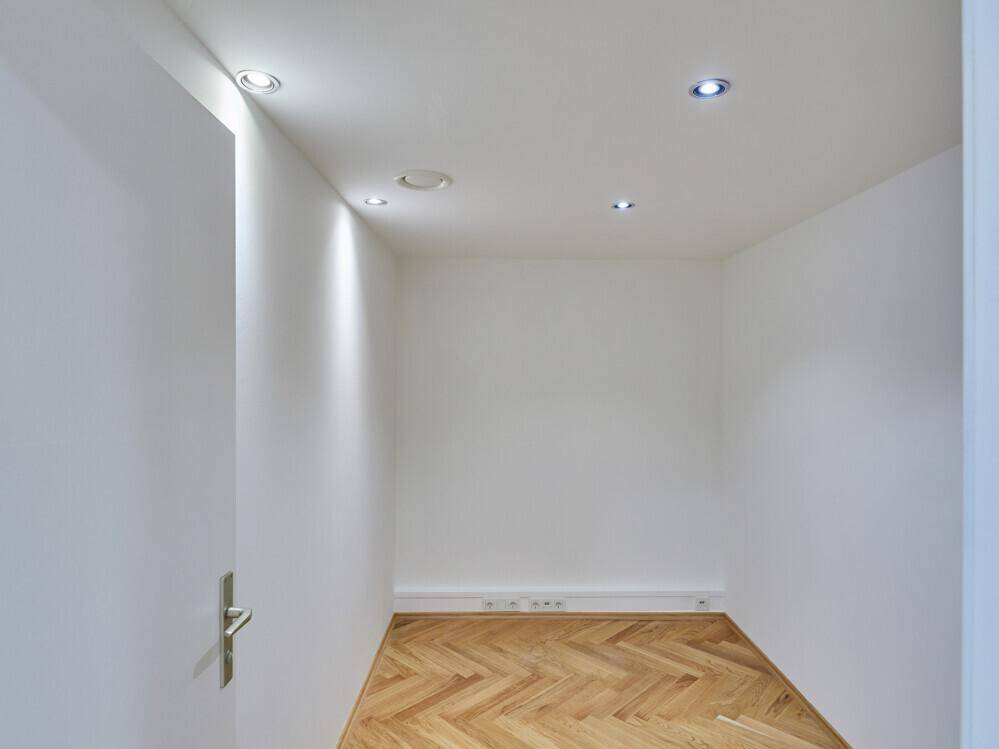 Kleiner, heller Büroraum mit Fischgrätparkett und Einbaustrahlern in der Decke.