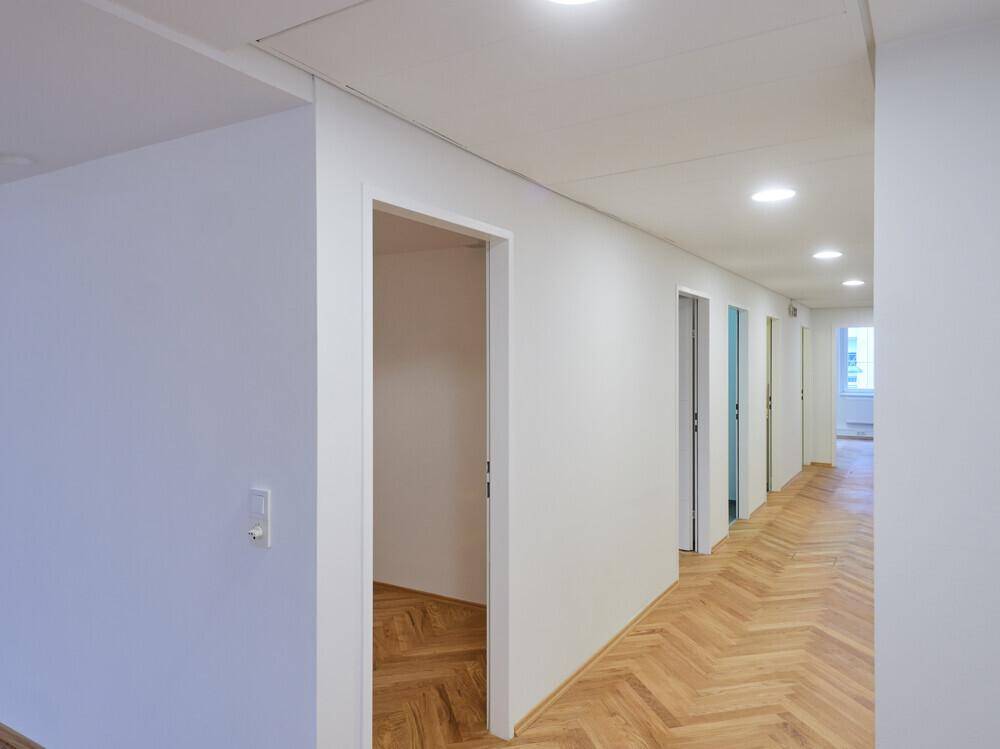 Langer, heller Flur mit Fischgrätparkett und mehreren Türen, die zu den Büroräumen führen.