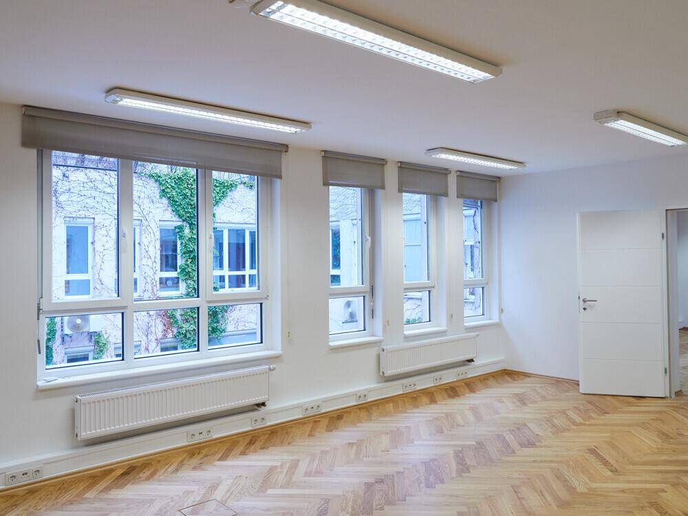 Büroraum mit großen Fenstern, die viel Tageslicht hereinlassen, und klassischem Fischgrätparkettboden.