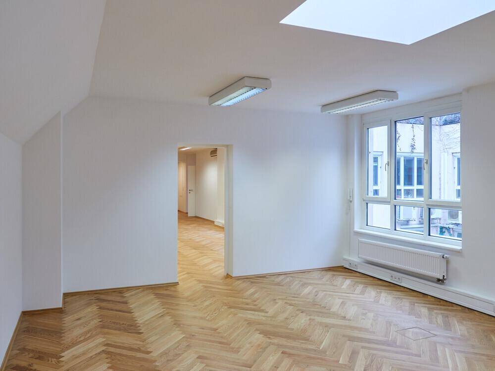 Heller Büroraum mit Fischgrätparkett, großen Fenstern und Blick auf den Innenhof.