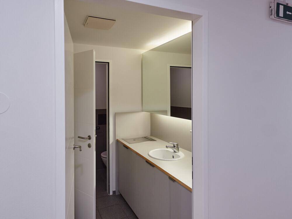 Modernes Gäste-WC mit Waschtisch, Spiegel und Zugang zu einer weiteren Toilette.