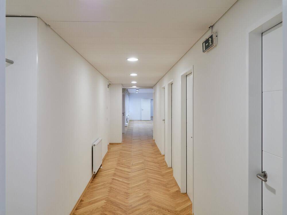 Langer, heller Flur mit Fischgrätparkett, Einbaustrahlern und mehreren Türen zu den Räumen.