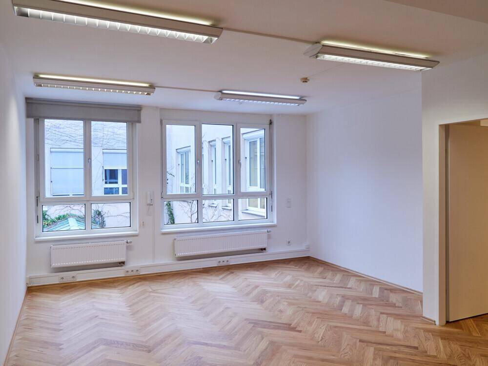 Heller Büroraum mit Fischgrätparkett, großen Fenstern und Blick auf den begrünten Innenhof.
