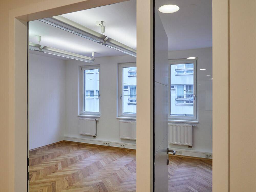Heller Büroraum mit großen Fenstern, die viel Tageslicht hereinlassen, und Blick auf die umliegenden Gebäude.