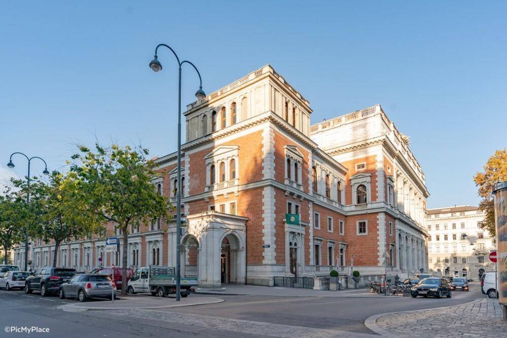 Historisches Eckgebäude mit roter Ziegelfassade und hellen Steinelementen an einem sonnigen Tag in urbaner Umgebung.