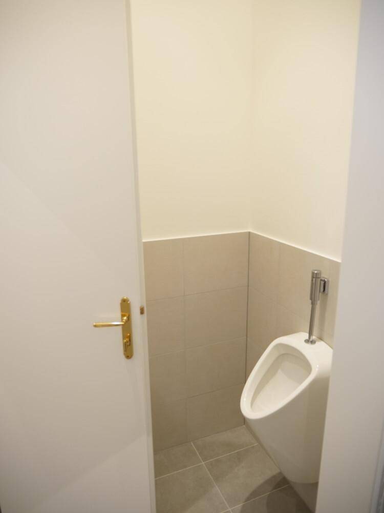 Gäste-WC mit modernem Urinal, hellen Fliesen und weißer Tür.