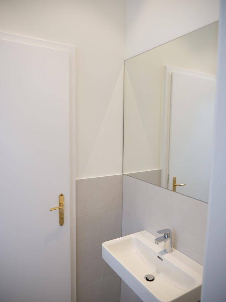Modernes Gäste-WC mit wandhängendem Waschbecken, großem Spiegel und hellen Fliesen.