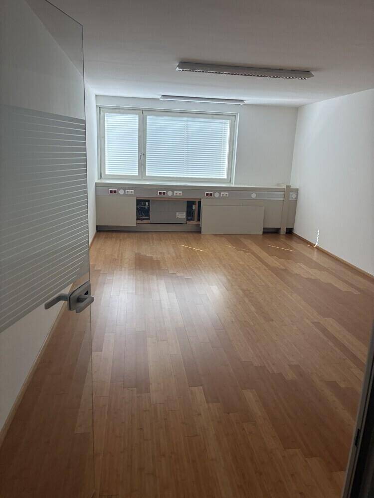Heller Büroraum mit Holzboden, großem Fenster und praktischen Einbauschränken entlang der Wand.