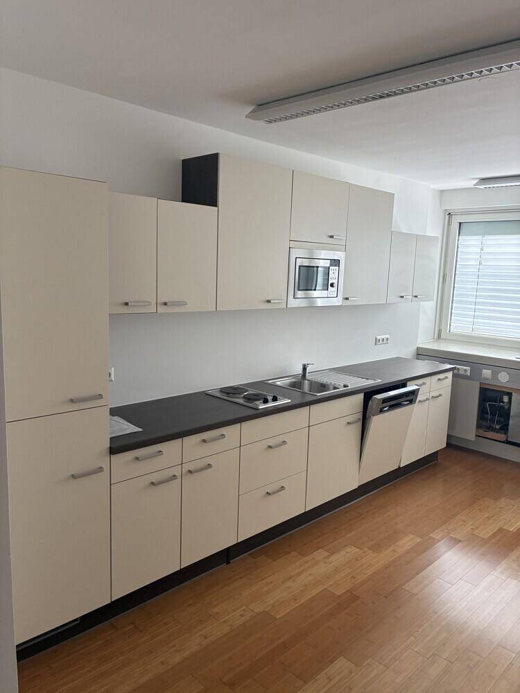 Funktionale Teeküche mit hellen Schränken, Spüle, Kochfeld, Mikrowelle und Geschirrspüler.