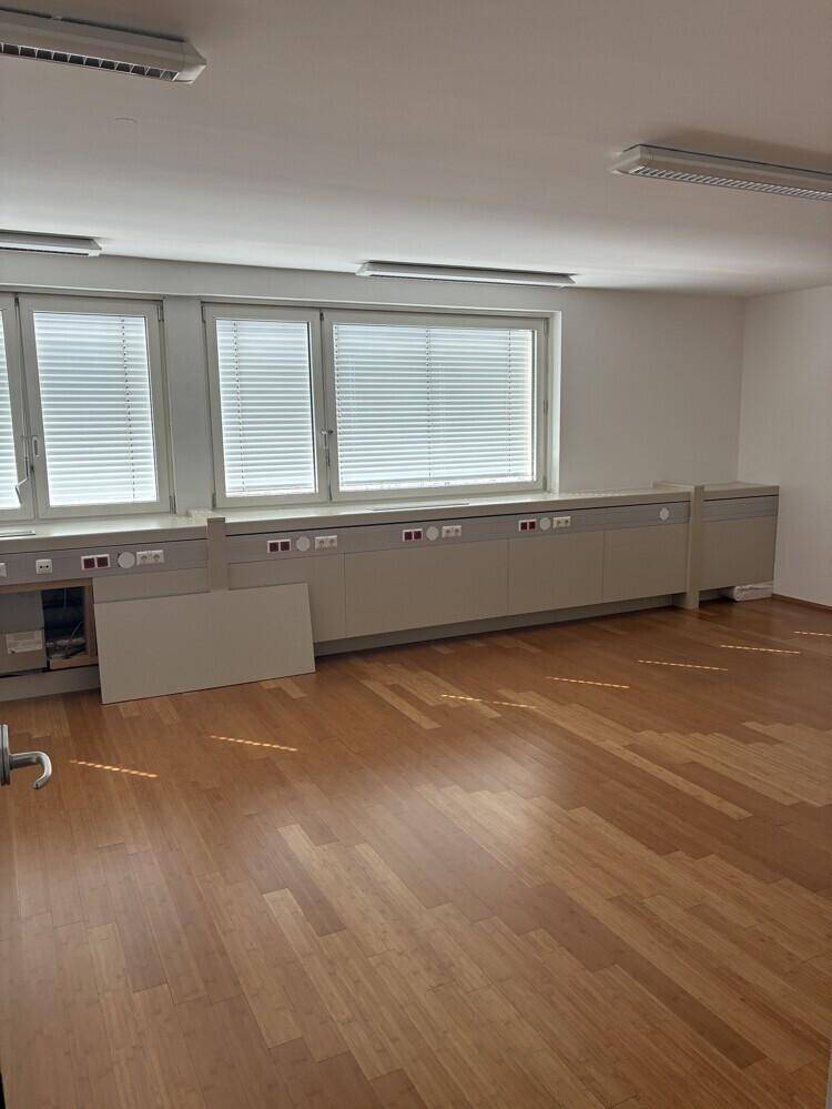 Heller Büroraum mit Holzboden, zwei Fenstern und einer langen Reihe von integrierten Schränken.