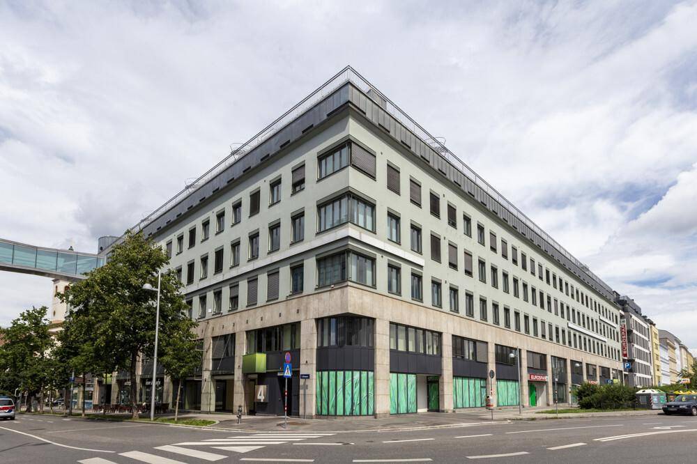 Großes, modernes Geschäftsgebäude an einer belebten Kreuzung mit vielen Fenstern und einer klaren Architektur.