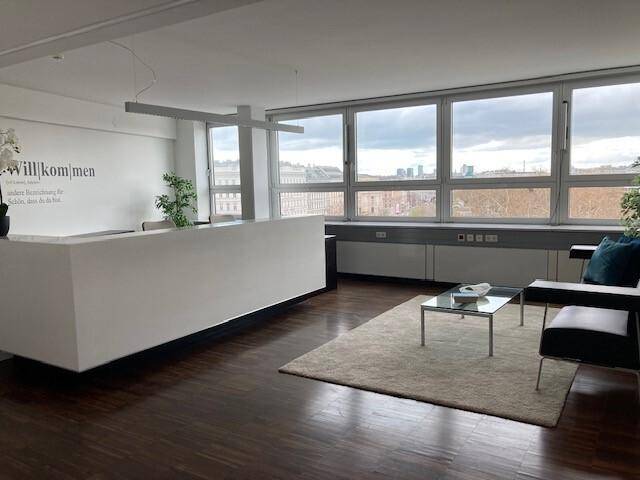 Moderner Empfangsbereich im Büro mit weißem Tresen, Loungesesseln und dunklem Holzfußboden.