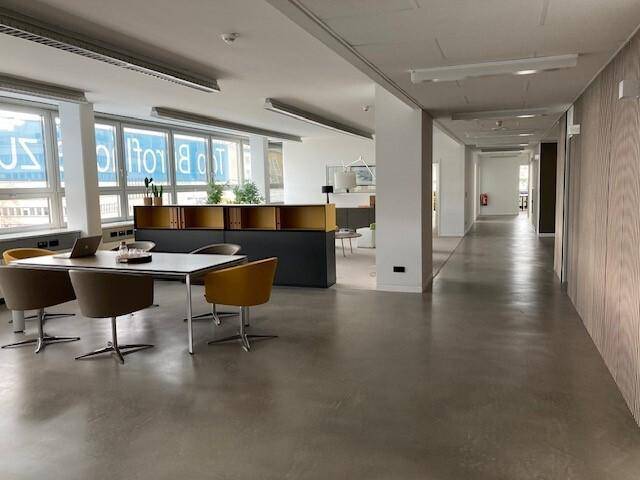 Offener Bürobereich mit langen Fluren, Schreibtischen und Stühlen, ausgestattet mit Betonboden.