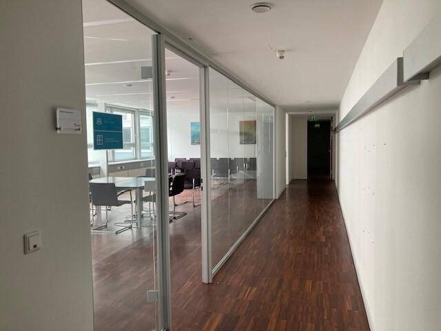 Büroflur mit Glasabtrennungen, die zu Besprechungsräumen führen, ausgestattet mit Holzfußboden.