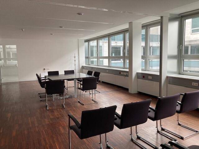 Büroraum für Besprechungen oder Schulungen mit mehreren Stühlen und Tischen, Holzfußboden.