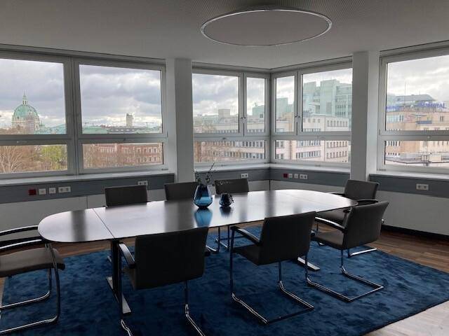 Konferenzraum mit ovalem Tisch, Stühlen und blauem Teppich, mit Stadtblick aus den Fenstern.