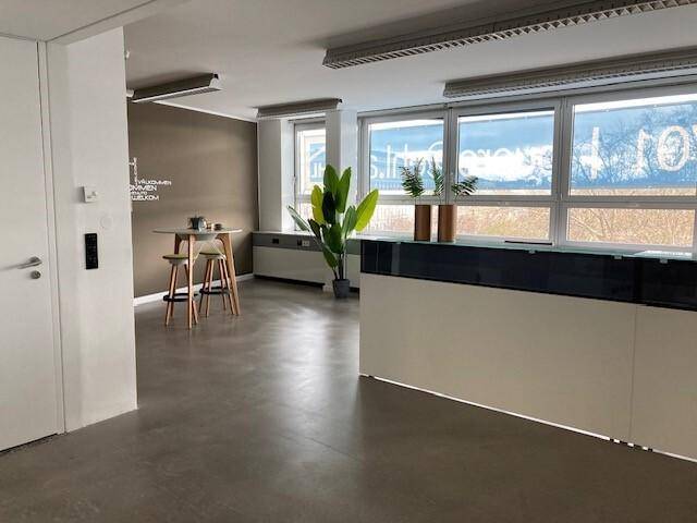 Moderner Empfangs- oder Loungebereich im Büro mit Stehtisch, Hockern und großen Fenstern.