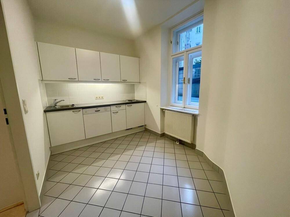 Kleine Küche mit weißen Einbauschränken, Spüle und einem Fenster, das den Raum mit Licht füllt.