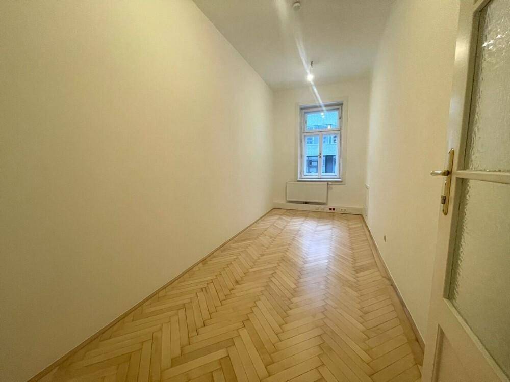 Leerer, schmaler Raum mit Fischgrätparkett und einem Fenster, das für natürliches Licht sorgt.