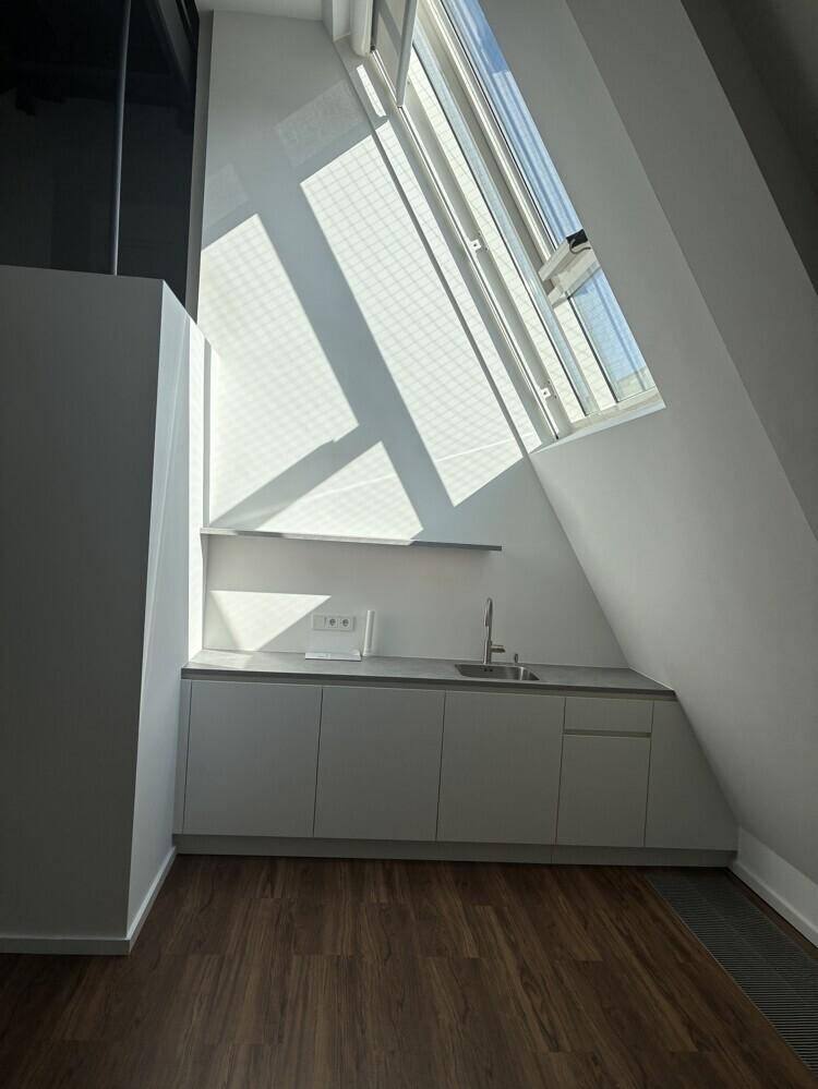 Kleine, moderne Küchenzeile mit Spüle und Unterschränken unter einem schrägen Dachfenster.