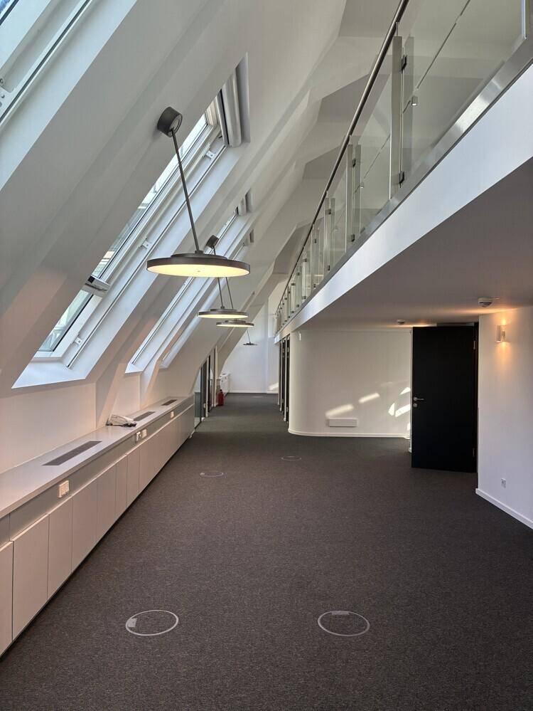 Heller Büroraum im Dachgeschoss mit schrägen Wänden, Dachfenstern und Teppichboden.