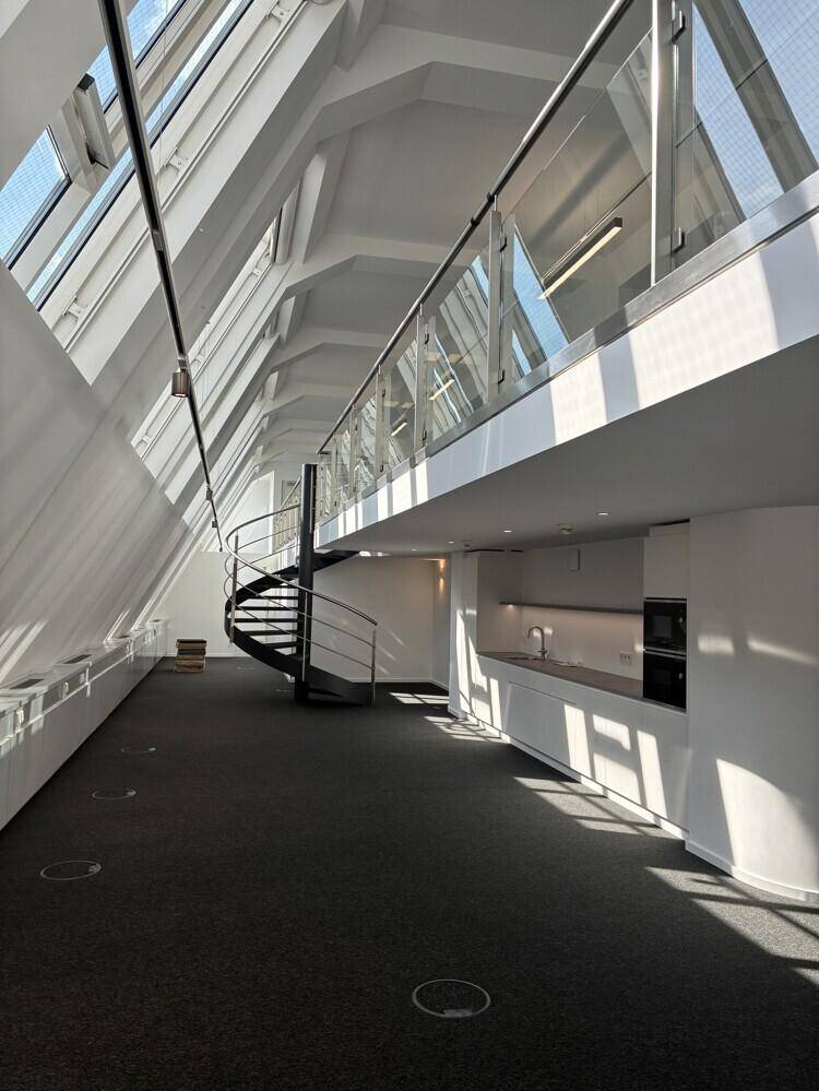 Offener Bürobereich mit integrierter Küchenzeile, Wendeltreppe und viel Tageslicht durch Dachfenster.