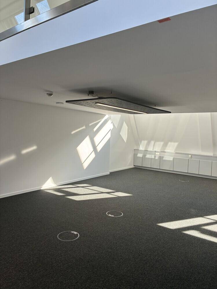Leerer Büroraum mit Teppichboden und interessanten Lichtmustern durch die Dachfenster.