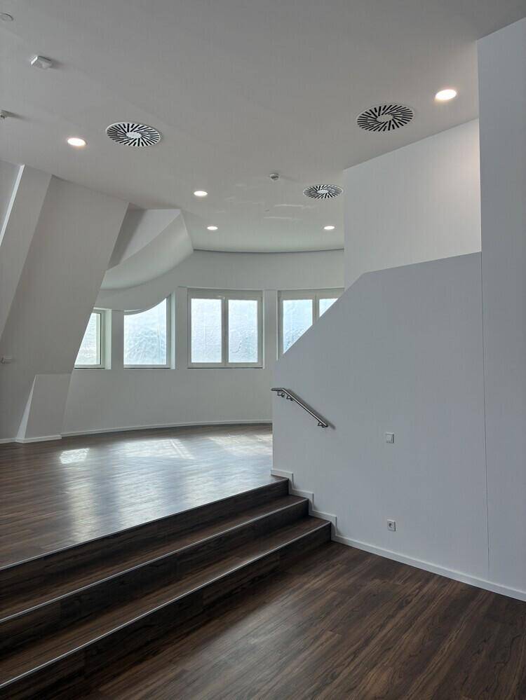 Heller Büroraum mit dunklem Holzboden, runden Fenstern und moderner Deckenbeleuchtung.