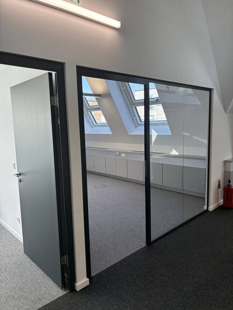 Büro mit modernen Glastüren, die den Blick auf weitere Räume und Dachfenster freigeben.
