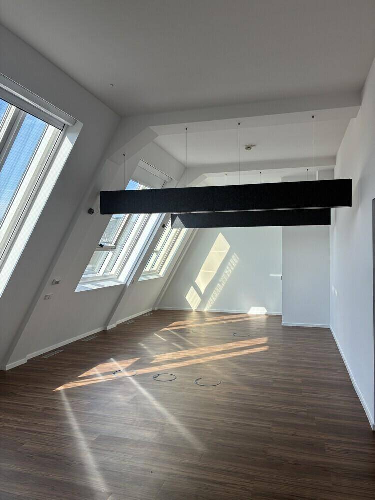 Großzügiger Büroraum mit Holzboden, schrägen Wänden und großen Dachfenstern für viel Helligkeit.