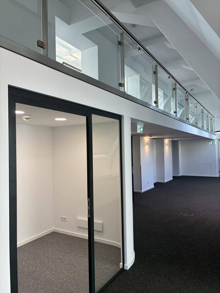Moderner Büroraum mit Glasabtrennungen und Blick auf die obere Etage mit Glasgeländer.