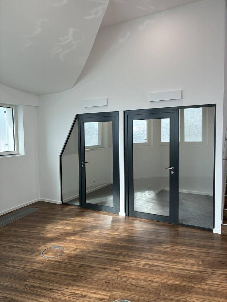 Büroraum mit eleganten Glastüren und warmem Holzboden, der viel Licht hereinlässt.