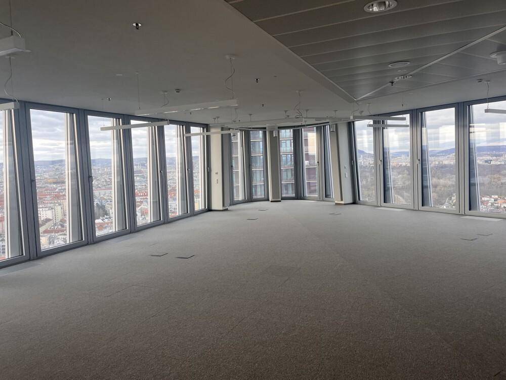 Geräumiger, leerer Büroraum mit bodentiefen Fenstern und weitem Blick über die Stadt, ausgestattet mit grauem Teppichboden.