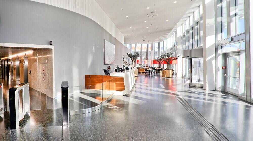 Geräumige und helle Lobby mit hoher Decke, Rezeption, Aufzügen und viel natürlichem Licht durch große Fenster.