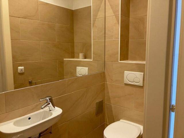 Moderne Toilette mit beigefarbenen Fliesen, integriertem Spiegel und wandhängendem WC.