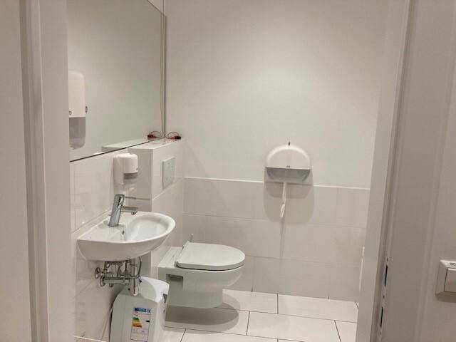 Helle Toilette mit weißem Waschbecken, wandhängendem WC und Fliesenboden.