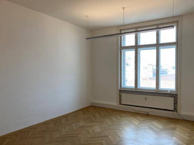 Heller, leerer Raum mit Fischgrätparkett, hohen Decken und großen Fenstern.