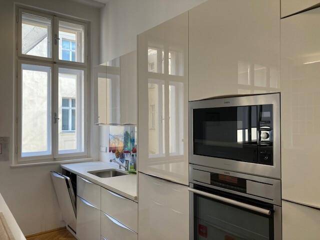 Moderne weiße Küche mit Hochglanzfronten, integrierten Geräten und Fensterblick.