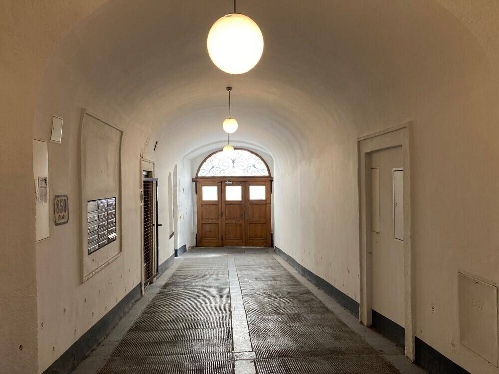 Langer, gewölbter Eingangsbereich mit Holztüren am Ende und Deckenleuchten, typisch für Altbauten.