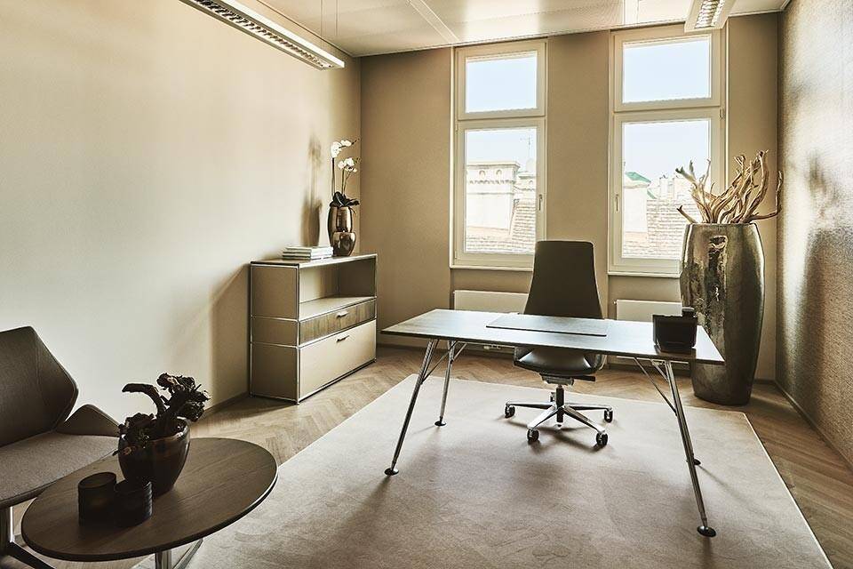 Helles und modernes Büro mit einem Schreibtisch, Bürostuhl, einem Aktenschrank und großen Fenstern mit Blick nach draußen.