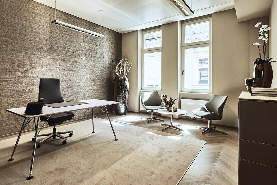 Geräumiges Büro mit modernem Schreibtisch, bequemen Besucherstühlen und einer strukturierten Wandverkleidung für eine stilvolle Atmosphäre.