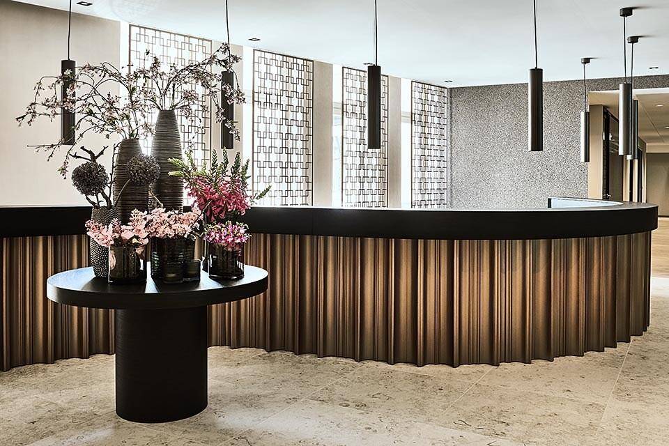 Elegante Empfangstheke mit geschwungener Form und floralen Dekorationen in einem modernen Eingangsbereich mit stilvoller Beleuchtung.