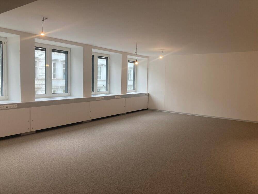 Heller Büroraum mit mehreren Fenstern, die viel Tageslicht hereinlassen, und Teppichboden.